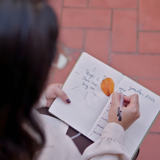 Mujer escribiendo en un cuaderno con una hoja seca, representando reflexión y transformación a través del coaching emocional.