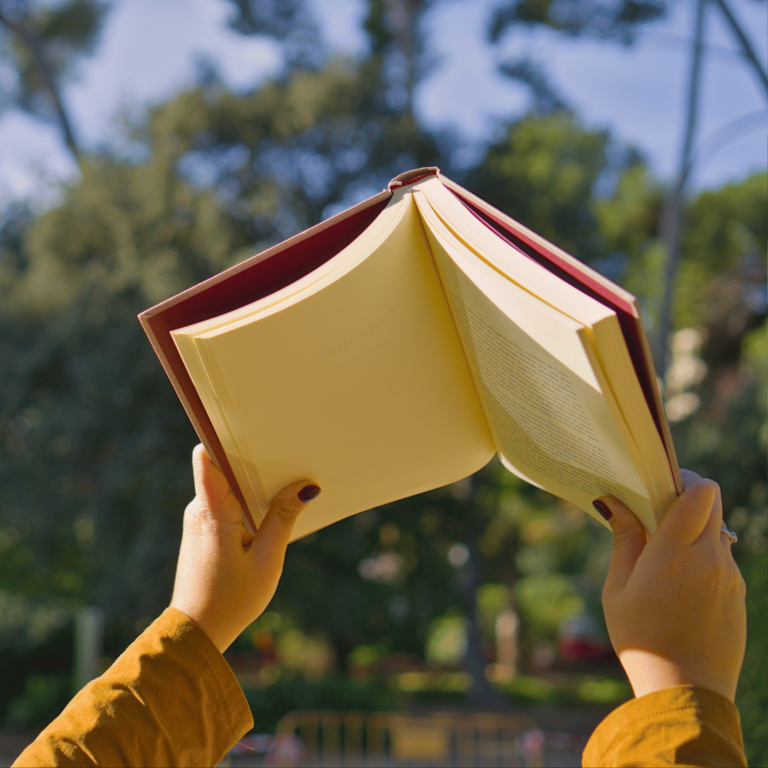 Manos sosteniendo un libro abierto al aire libre, representando crecimiento y transformación personal.